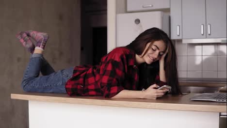 Slowmotion-footage-of-a-young-girl-smiling-and-laughing-whilelying-on-her-kitchen-table-surface-and-texting-someone.