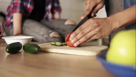 Slow-motion-close-up-of-a-young-playful-mulatto-guy-cutting-tomato-for-salad,-making-lunch-with-his-girlfriend-beside-him.-Relationship-goals.