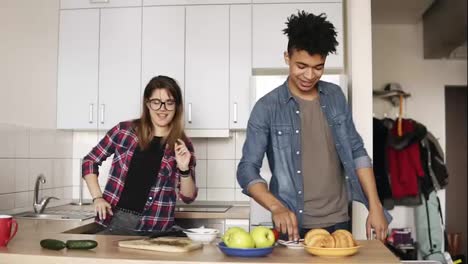 A-couple-of-two-playful-young-people,-with-urban-modern-hipster-stylish-outfits,-enjoying-their-time-together,-dancing-in-the-kitchen.-Living-together-goals.