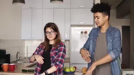 Attractive-caucasian-girl-with-stylish-hipster-glasses-and-playful-mulatto-guy,-both-in-ther-20's,-dancing-in-the-kitchen,-enjoying-youth,-having-fut-time-together.