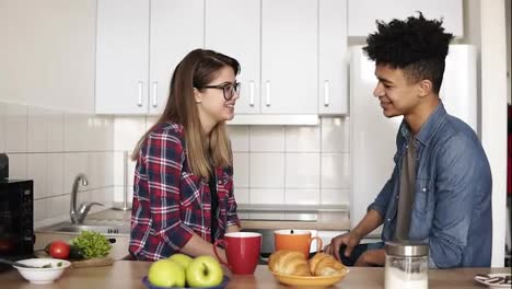 Tender,-caring-mulatto-guy-tucks-his-happy-caucasian-girlfriend's-hair-behind-her-ear,-they're-having-interesting-conversation-in-the-kitchen.-Couple-goals,-enjoying-time-together.