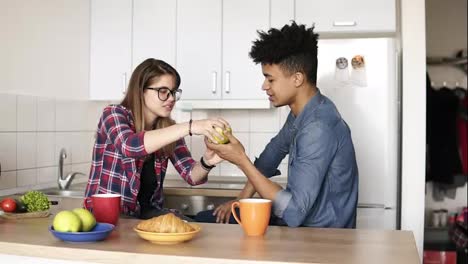Cute-couple-eating-apple-together,-sitting-in-their-spacious-well-lit-comfy-kitchen.