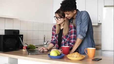 Slow-motion-footage-of-a-cute-couple-surfing-the-web,-using-laptop-while-sitting-in-a-kitchen