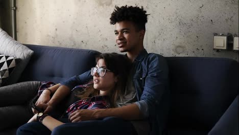 Cute-happy-couple-of-young-hipsters-lying-on-the-couch,-making-silly-faces,trying-to-find-a-perfect-tv-channel.-Leisure-time,-enjoying-youth,-living-together.-Relationship-goals.
