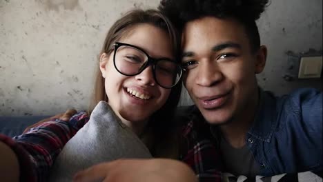 Young-cute-happy-couple,-attractive-caucasian-girl-and-handsome-mulatto-guy-cuddling-and-kissing-while-looking-at-the-camera.