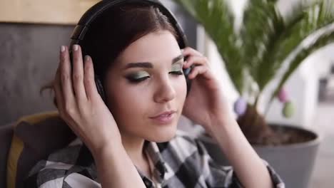 A-brunette-girl-with-a-beautiful-make-up,-puts-on-headphones-and-listens-with-pleasure-to-her-favorite-music.-Gestures-with-his-hands.-Close-up