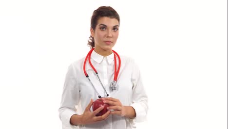 Young-nutritionist-holding-red-apple,-advising-healthy-diet.-Friendly-female-doctor-showing-red-apple-smiling.-Portrait-of-young-professional-with-stethoscope-and-lab-coat-isolated-on-white-background