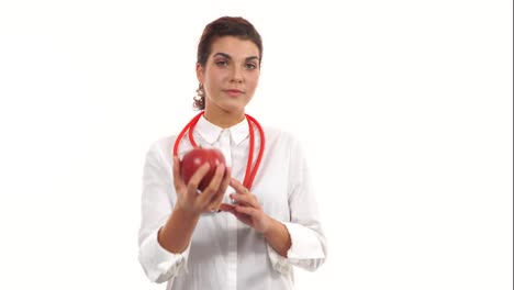 Young-friendly-female-nutritionist-showing-a-red-apple,-advising-healthy-diet.-Portrait-of-young-professional-with-stethoscope-and-lab-coat-isolated-on-white-background