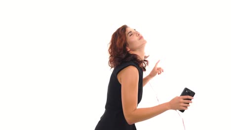 Joyful-young-girl-in-black-dress-listening-to-the-music-with-her-earphones-and-having-fun-dancing-isolated-on-the-white-background