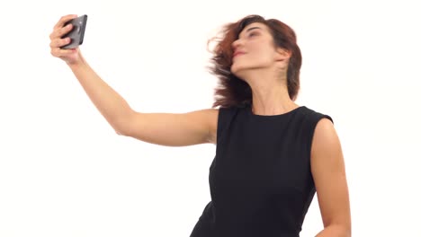 Young-attractive-caucasian-woman-shaking-her-head-making-selfie-on-mobile-phone-and-showing-peace-gesture-isolated-over-white