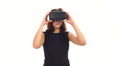 Attractive-young-woman-in-black-dress-taking-on-and-wearing-virtual-reality-glasses-isolated-over-white