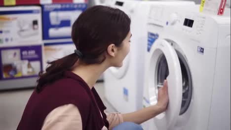 Young-brunette-girl-opens-a-washing-mashine-door,-spins-the-cylinder-inside-and-pulls-out-detergent-tray.-Costumer-looking-for-household-equipment.-Home-appliance.