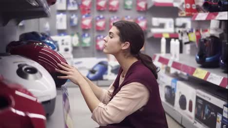 Girl-choosing-new-vacuum-cleaner-in-appliance-store.-Costumer-examining-domestic-equipment.