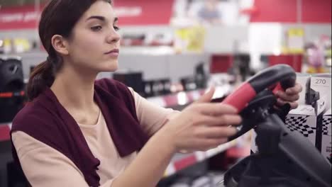 Young-beautiful-female-costumer-choosing-racing-weel-for-PS4-in-department-of-electronics-in-appliance-store.