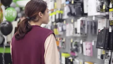 Backside-footage-of-a-brunette-girl-taking-a-box-with-headphones-from-display-in-electronics-store