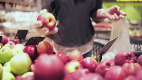 Woman-choosing-red-apples-at-the-grocery-store.-Womans-hand-picks-out-apples-at-the-fruit-and-vegetable-aisle-in-a-supermarket