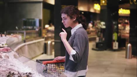 Young-female-costumer-trying-to-choose-seafood-at-a-supermarket.-Walking-along-the-row