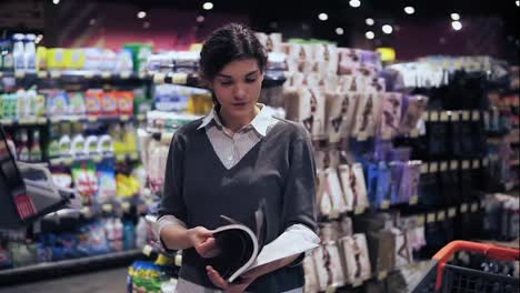 Young-beautiful-brunette-girl-at-her-20's-leafing-through-magazine-in-local-supermarket