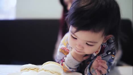 An-adorable-cute-asian-toddler-boy-enjoys-eating-macaroons-with-his-mother-sitting-beside-him.