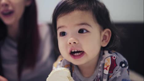 An-adorable-cute-asian-toddler-boy-is-eating-cookie-beside-his-young-mother-with-red-hair.