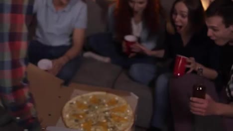 Happy-friends-got-delivery-pizza-and-celebrating-party-clinking-bottles-and-red-cups-with-beer-and-soda-sitting-on-sofa-at-home.-So-excited-about-big-pizza-party