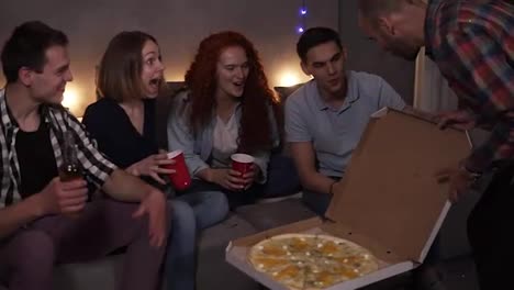 Cheerful-friends-got-delivery-pizza-and-celebrating-party-clinking-bottles-and-red-cups-with-beer-and-soda-sitting-on-sofa-at-loft-room.-So-excited-about-big-pizza-party.-Slow-motion