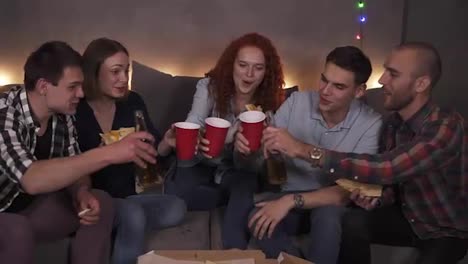 Portrait-of-diverse-group-of-friends-have-delivered-pizza-celebrating---happily-drinking-beer,-cheers.-Having-fun-party-in-cozy-room-decorated-with-garland-lights-in-a-company-of-close-friends