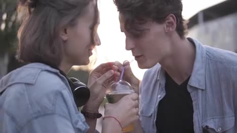 Closeup-view-of-attractive-young-couple-in-the-park-standing-and-and-sharing-milkshake-drinking-it-together-using-two-straws