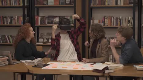 The-boy-in-plaid-shirt-is-wearing-virtual-reality-glasses-in-the-college-library-among-his-classmates.-The-concept-of-modern-technologies-and-virtual-life-in-education