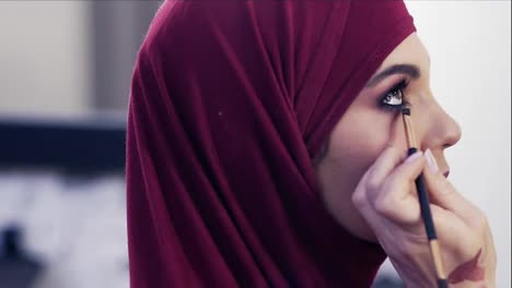 Adding-some-more-eyeliner-on-the-waterline-of-a-gorgeous-girl's-eyes.-Stunningly-beautiful-female-wearing-purple-hijab