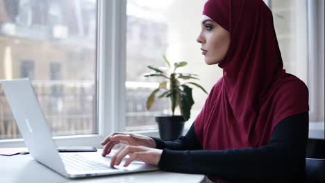 Young-attractive-supposedly-muslim-girl-typing-something-on-her-laptop.-Indoors-footage