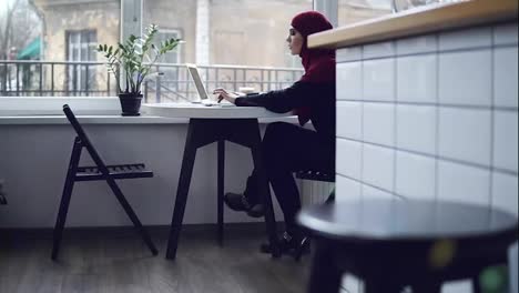 Beautiful-muslim-girl-with-hijab-on-her-head,sitting-near-the-window,-is-typing-down-something-on-the-keyboard-of-her-laptop