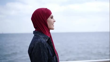 Una-Joven-Atractiva-Con-Hijab-En-La-Cabeza-Camina-Supuestamente-Cerca-De-La-Orilla-Del-Mar-Con-Gaviotas-Volando-En-El-Fondo