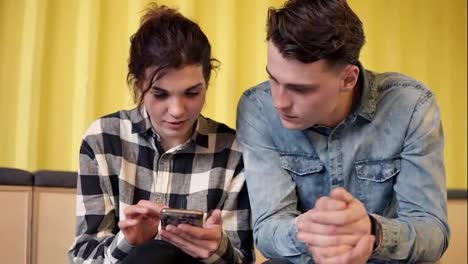A-couple-sitting-and-chatting-about-something.-Young-attractive-girl-shows-her-boyfriend-something-on-her-smartphone.