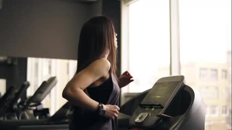 Attractive-brunette-girl-with-long-hair-in-her-20's-wearing-dryfit-sportswear,-running-on-treadmill.-Indoors-footage.
