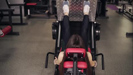 Backside-footage-of-a-sportive-brunette-girl-working-out-on-leg-press-at-the-gym.-Healthy-lifestyle,-fitness-and-recreation.
