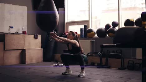 Young-brunette-girl-with-sportive-body-wearing-black-sportswear-doing-squats-at-the-gym.