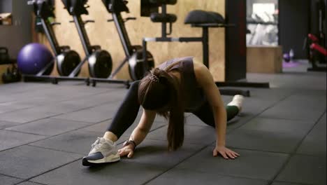 Attractive-brunette-female-in-her-20's-stretching-out-in-the-gym,-preparing-leg-muscles-to-do-the-splits.