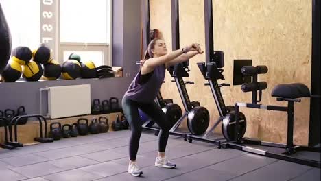 Attractive-slim-brunette-girl-wearing-dryfit-sportswear-doing-squats-in-the-gym-without-any-equipment.-Indoors-footage.-Healthy-lifestyle,-fitness-and-wellbeing.
