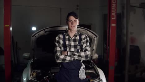 Portrait-of-young-handsome-car-mechanic-in-workshop,-in-the-background-of-service.-Car-repair,-fault-diagnosis,-technical-maintenance-concept