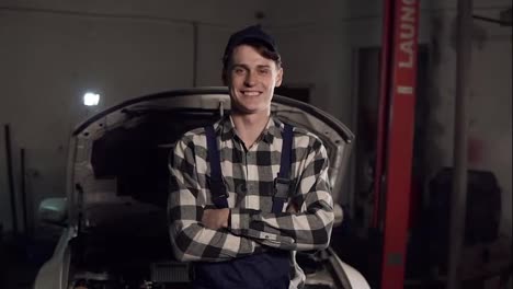 Portrait-of-young-handsome-car-mechanic-in-workshop,-in-the-background-of-service.-Car-repair,-fault-diagnosis,-technical-maintenance-concept.