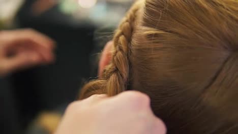 Hands-of-a-hairdresser,-she-is-plaiting-the-braid-for-fair-haired-model,-close-up