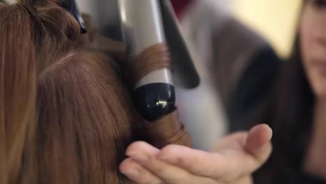 The-hairdresser-continues-curling-hair-to-a-beautiful-long-haired-girl-with-a-ploy.-Close-up