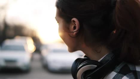 Side-view-of-a-girl-with-headphones-around-her-neck.-She-smiles,-turns-to-look-in-a-blurred-perspective.-Long-brown-haired