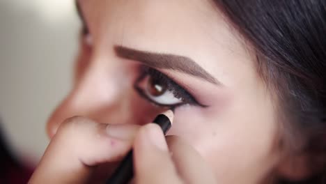 Professional-makeup-artist-lining-inner-eye-rim---working-in-beauty-fashion-industry-cosmetics-backstage-professional-make-up---macro-close-up-beautiful-natural-lighting.-Slow-motion.-High-angle-view