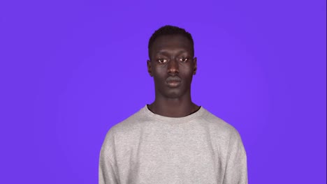 Front-view-portrait-of-young-serious,-calm-man-staring-at-camera.-Beautiful-african-black-man-in-white-sweatshirt-on-blue-background
