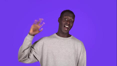 Say-hello-A-friendly-smiling-black-man-waves-affably-at-the-camera.-Standing-over-blue-background-and-waving-hi-gesture