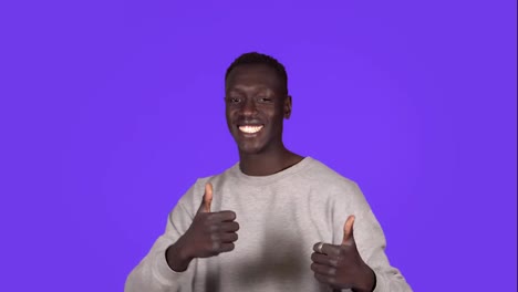 Young-african-american-man-smiling-and-dancing-in-good-mood-on-blue-background.-Unstoppable-fun,-happiness,-thumbs-up,-human-emotions