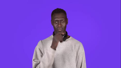 Afro-american-man-isolated-against-blue-background-with-headphones-on-neck-smelling-something-stinky-and-disgusting,-holding-breath-with-fingers-on-nose.-Bad-smells-concept