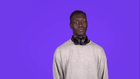 Clapping-young-african-man,-applauding-in-respect-to-someone.-Isolated-on-blue-background.-Wearing-white-sweater-and-headphones-on-neck